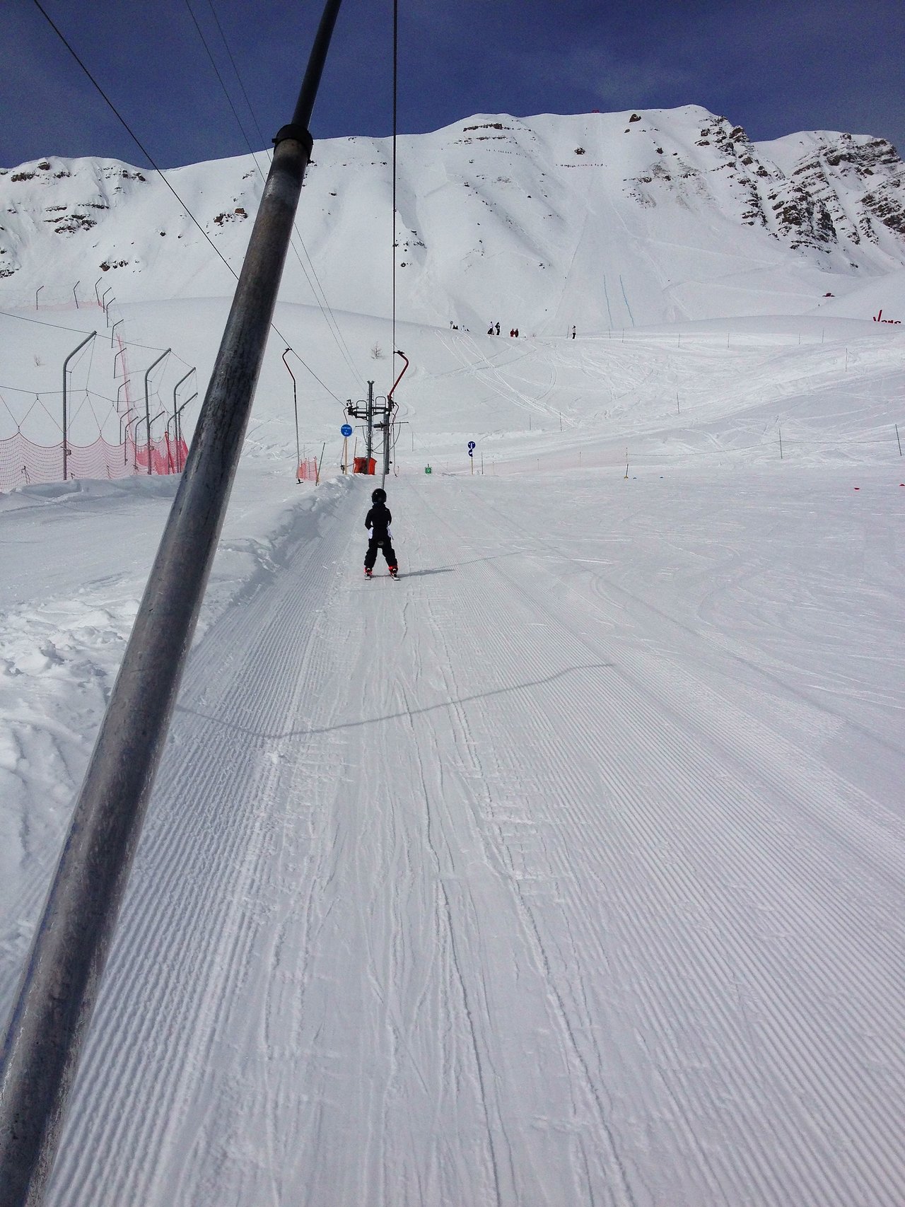 A person in ski gear rides a ski lift up a snowy mountain slope.