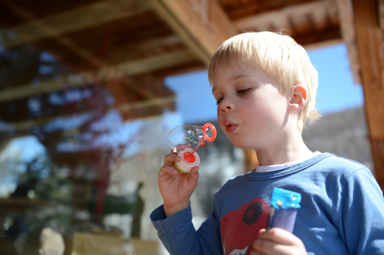 A young child blows bubbles using a small wand while holding a bottle of bubble solution.