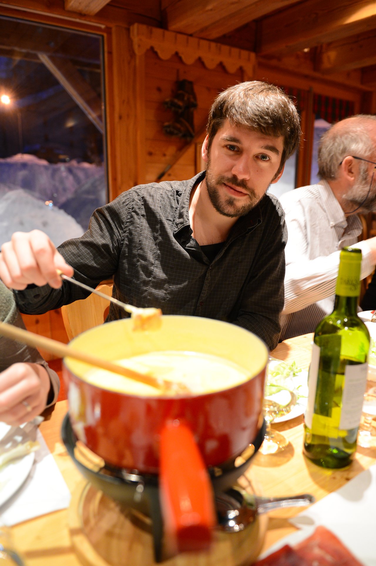 A man dips a piece of bread into a pot of melted cheese at a fondue dinner.