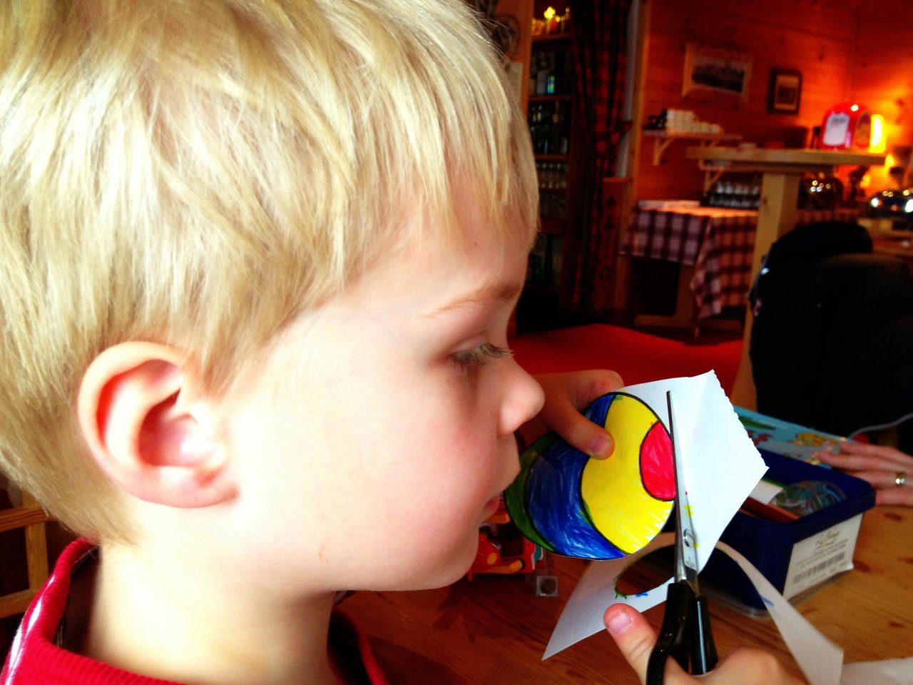A child carefully cuts out a colorful, hand-drawn shape from a piece of paper using scissors.