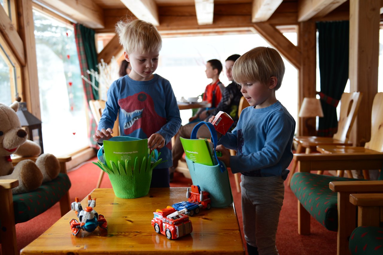 Two young children in blue shirts look through their Easter baskets, examining toys and treats on a wooden table.