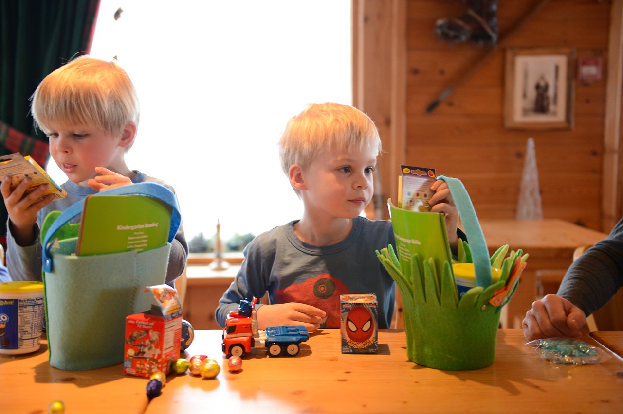Two young boys sit at a table, looking through their Easter baskets filled with toys, candy, and small gifts.