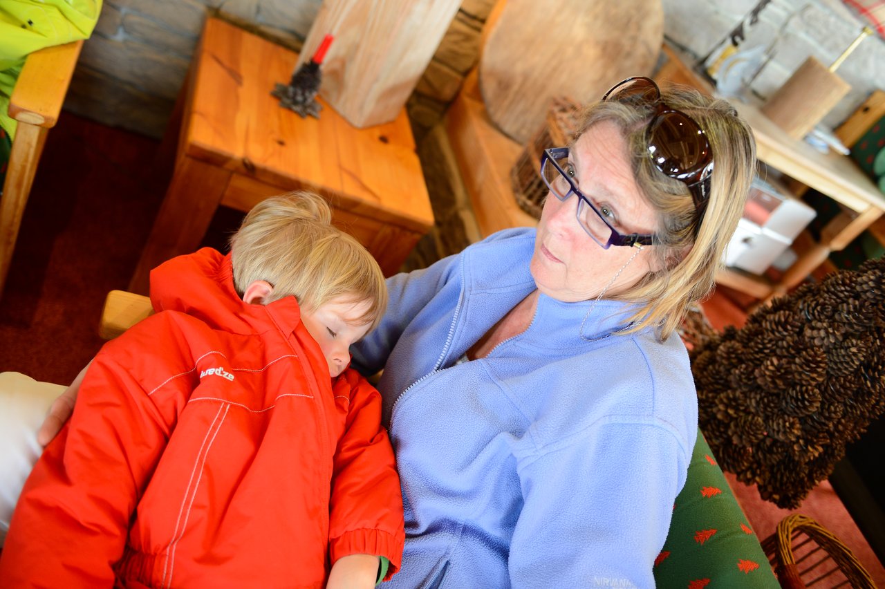 A child in a red jacket sleeps on a woman's lap while she looks off to the side.