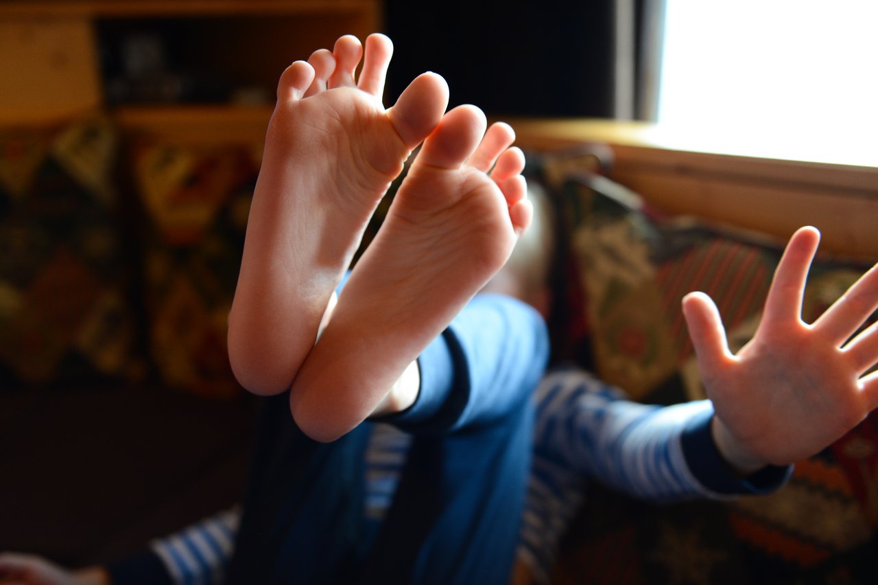 Close-up of bare feet raised toward the camera, with hands and a blurred person in the background.