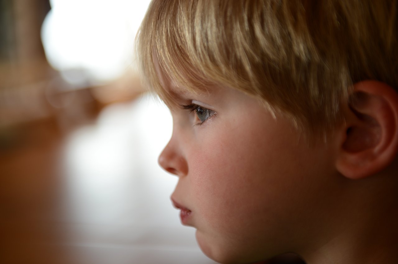 A young child with blond hair looks intently at something off-camera, appearing focused and deep in thought.