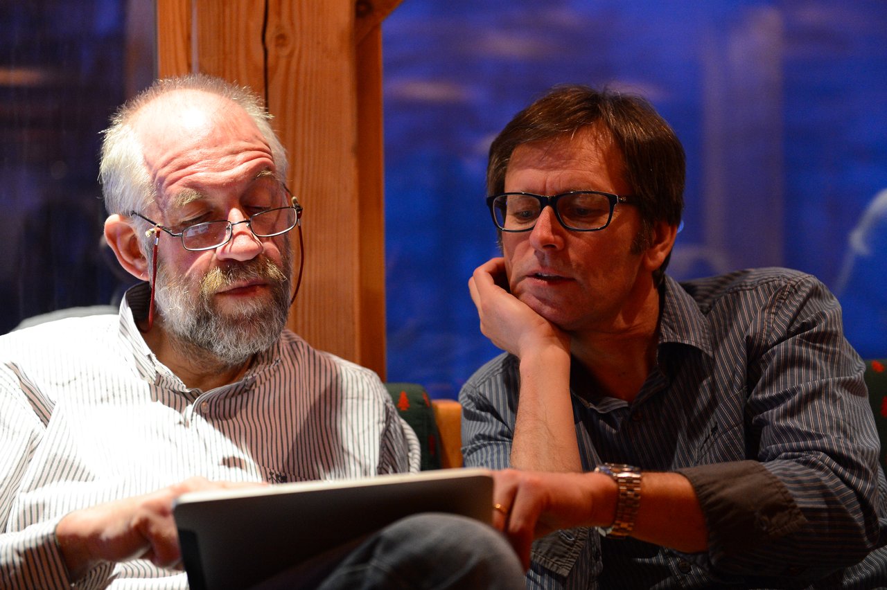 Two men sitting together, looking at an iPad.