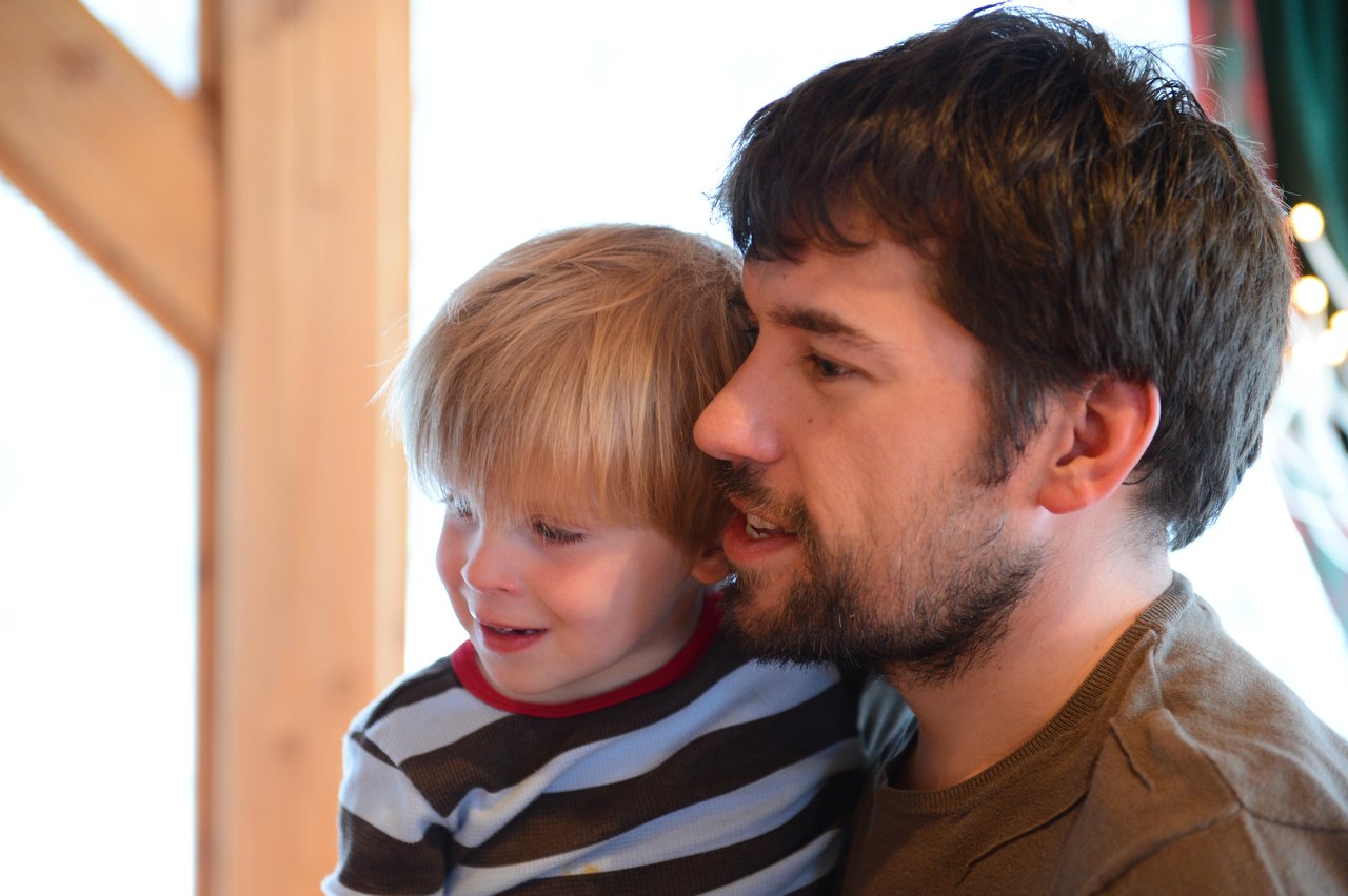 A man with a beard holds a young child in a striped shirt.