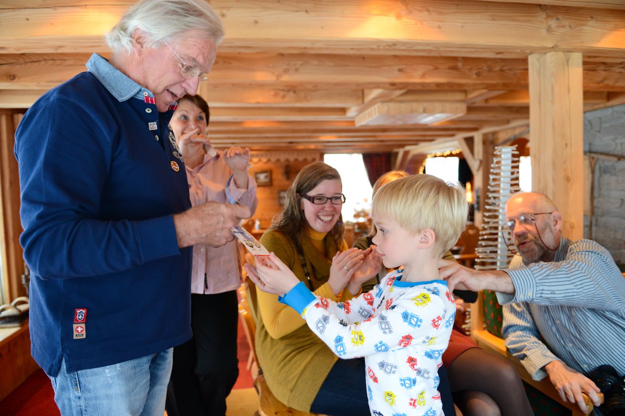 An older man hands a medal to a young child, while others in the room watch and smile.