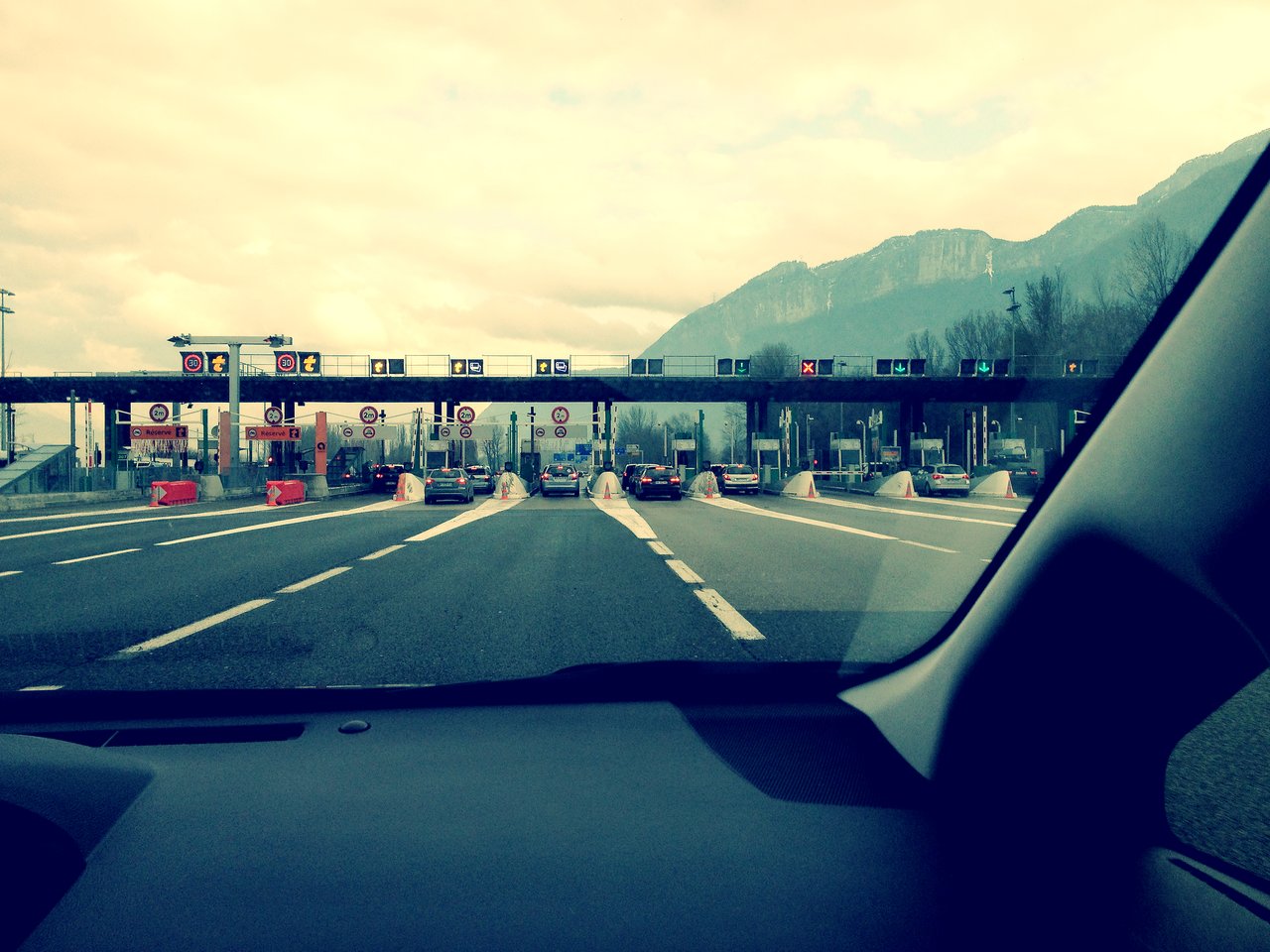 Cars approach a toll booth on a highway, viewed from inside a vehicle.