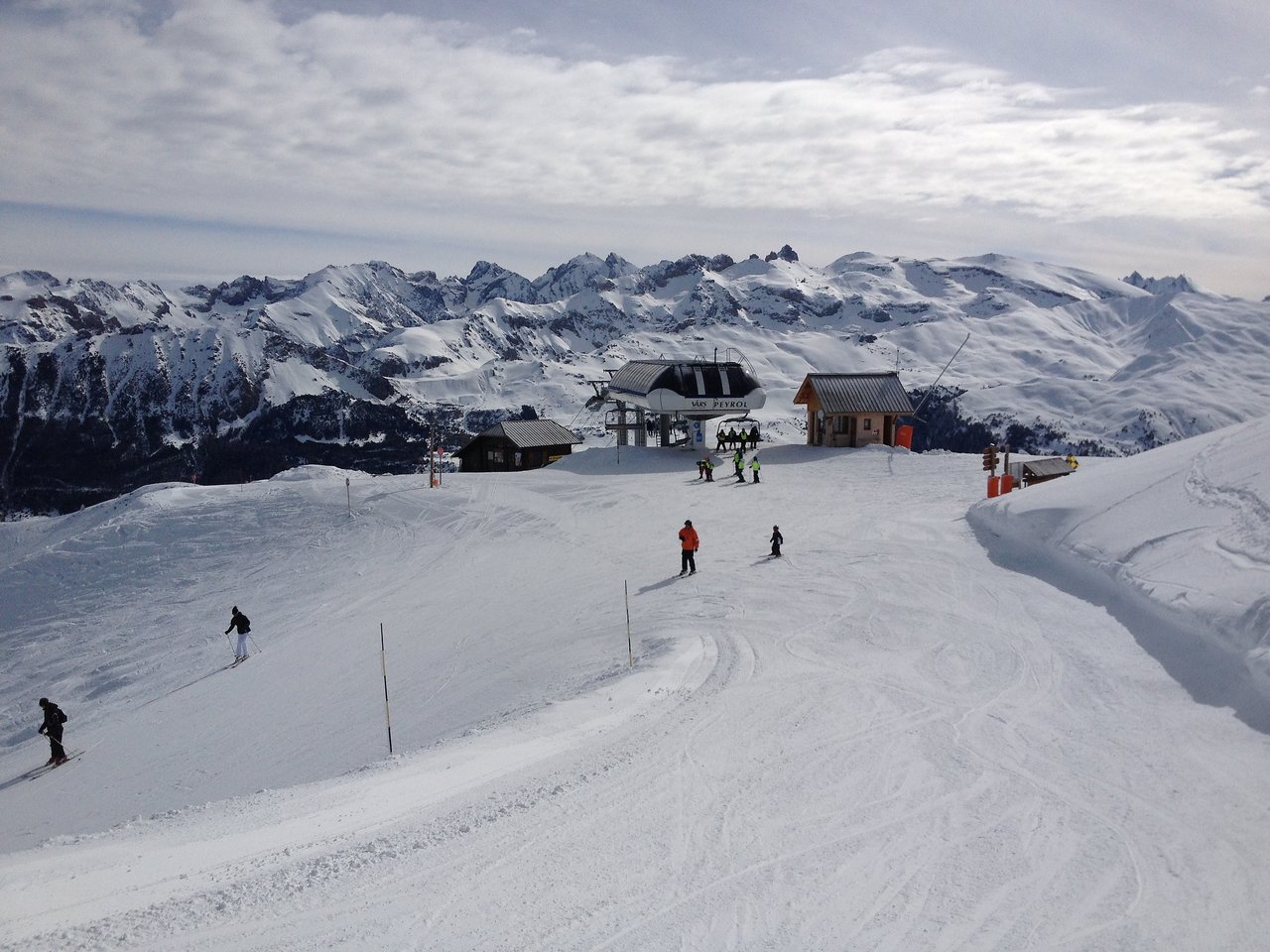 Two people skiing down a snowy slope near a ski lift, with others in the background.