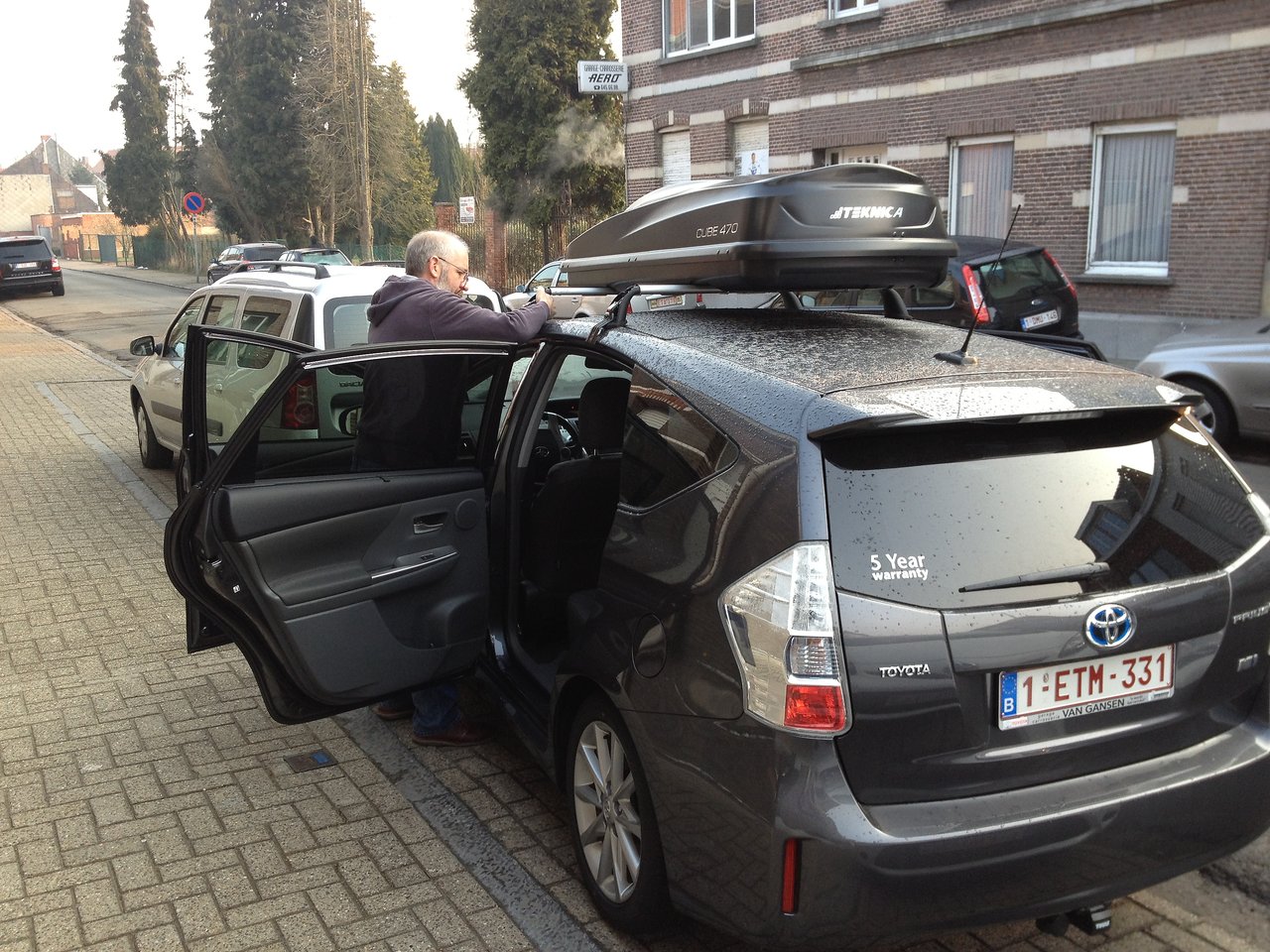 A person loads items into a rooftop cargo box on a black car with open doors.
