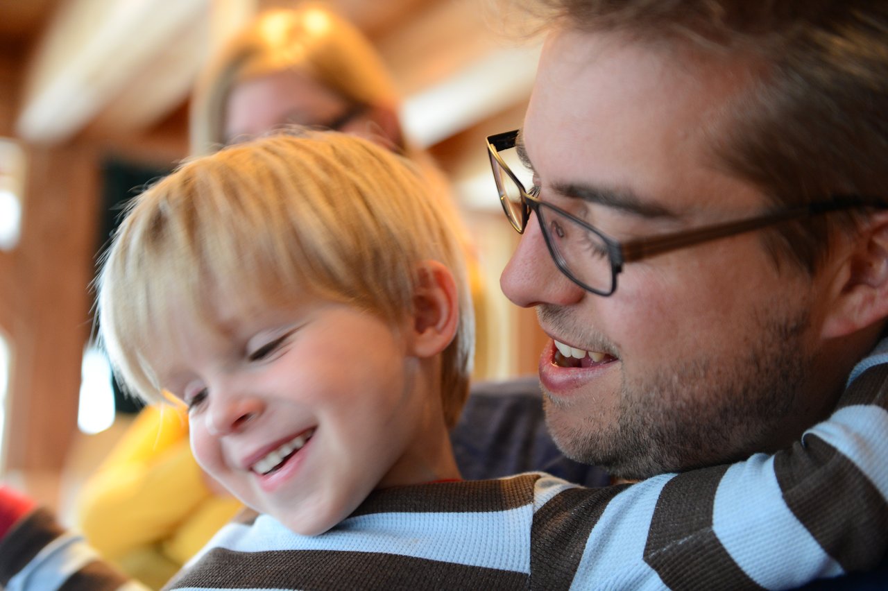 A father and his young son share a happy moment, smiling as they embrace each other closely.