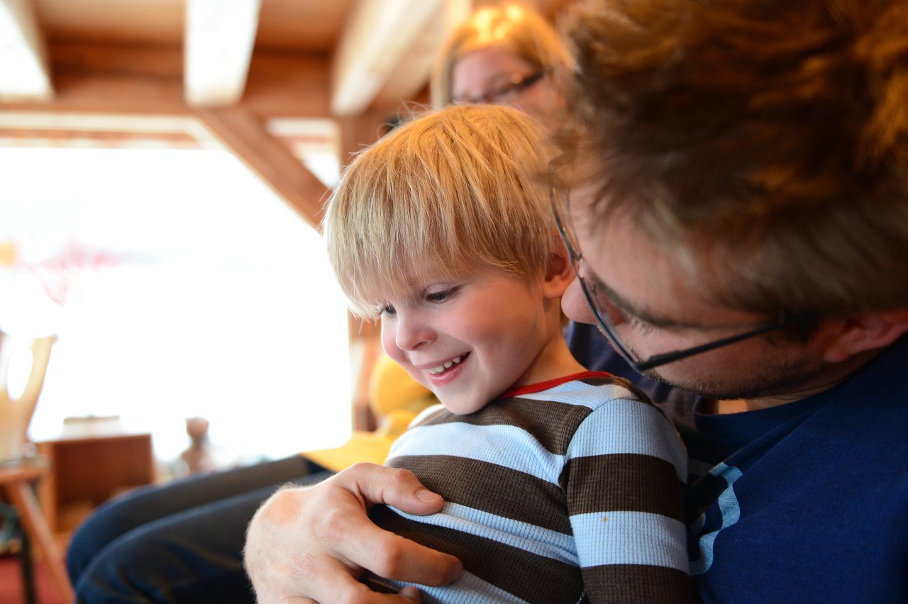 A father holds his young son, who is smiling and looking down.