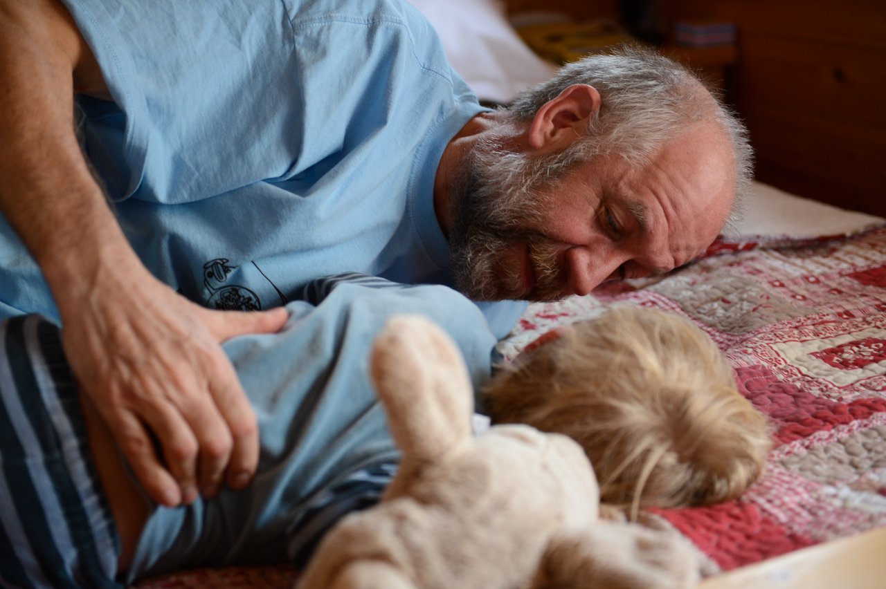 An older man and a young child lie on a bed, facing each other.