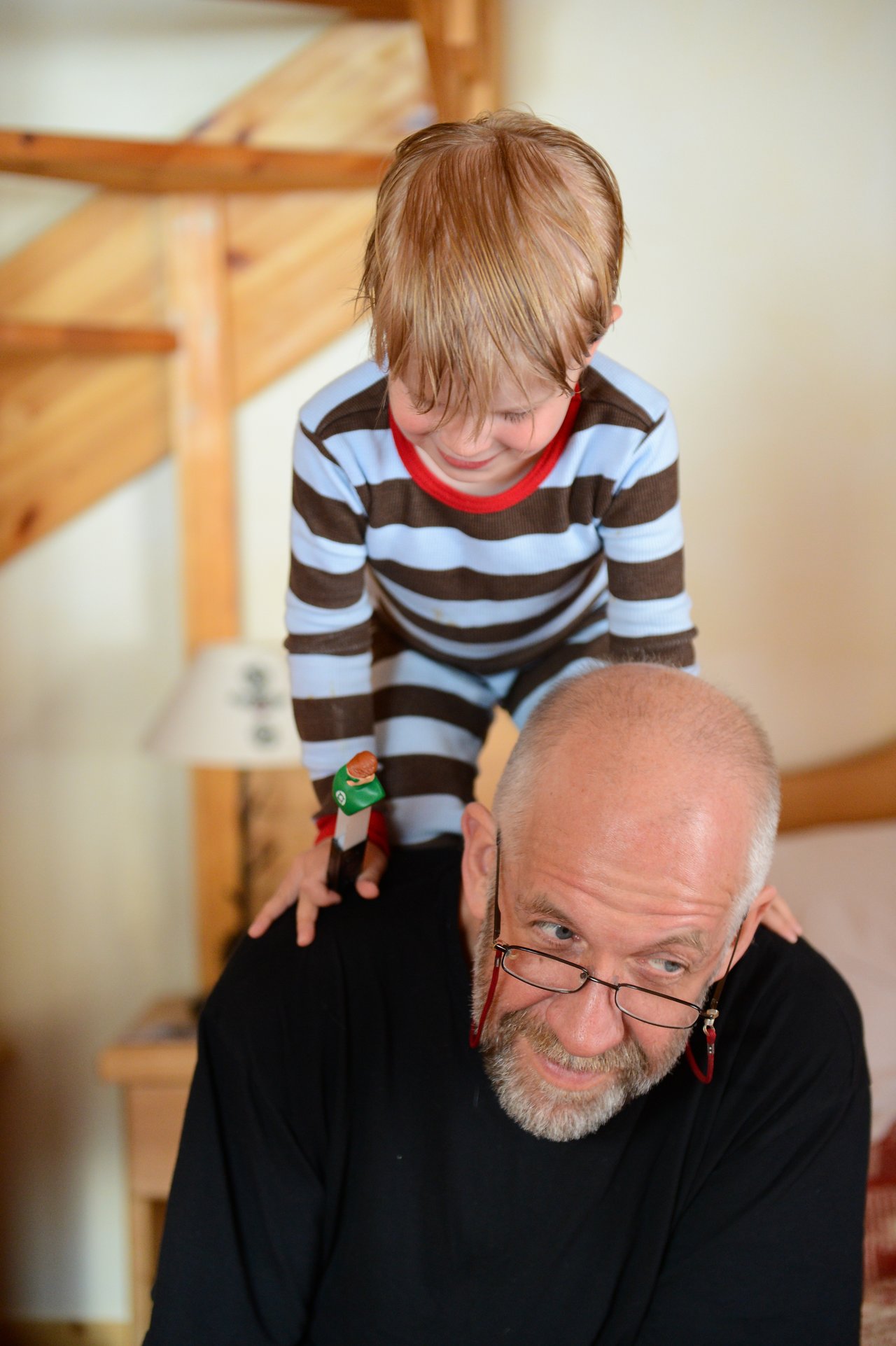 A young child in striped pajamas climbs onto an older man's back while holding a small toy figure.