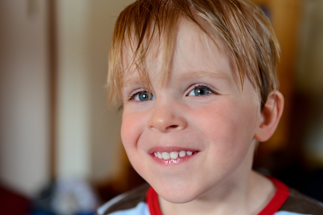 A young child with light brown hair smiles brightly, showing teeth, and appears to be giggling.
