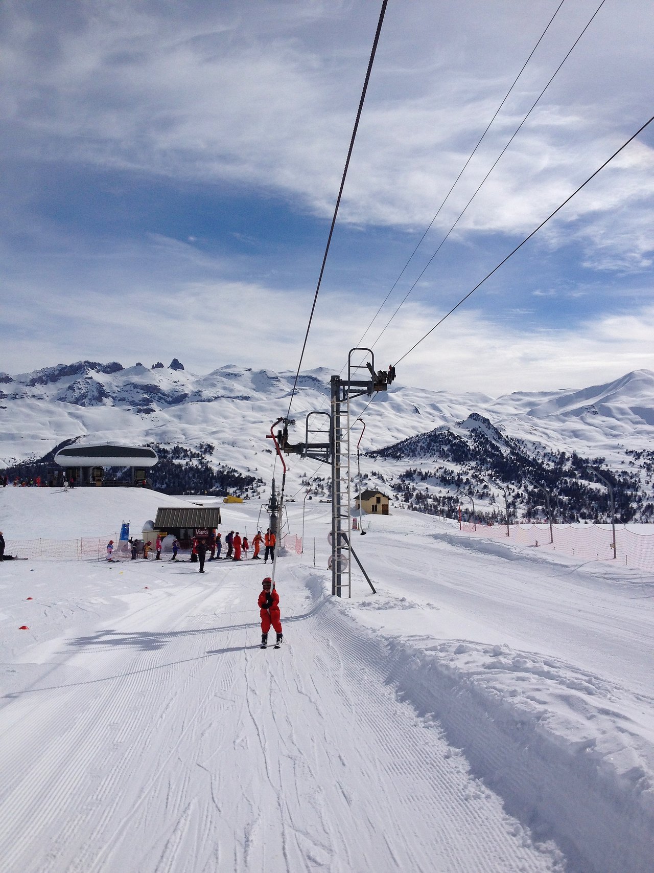 A child in a red ski outfit rides a ski lift alone for the first time on a snowy slope.