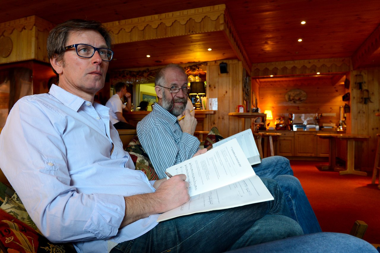 Two men sit together, reviewing documents.