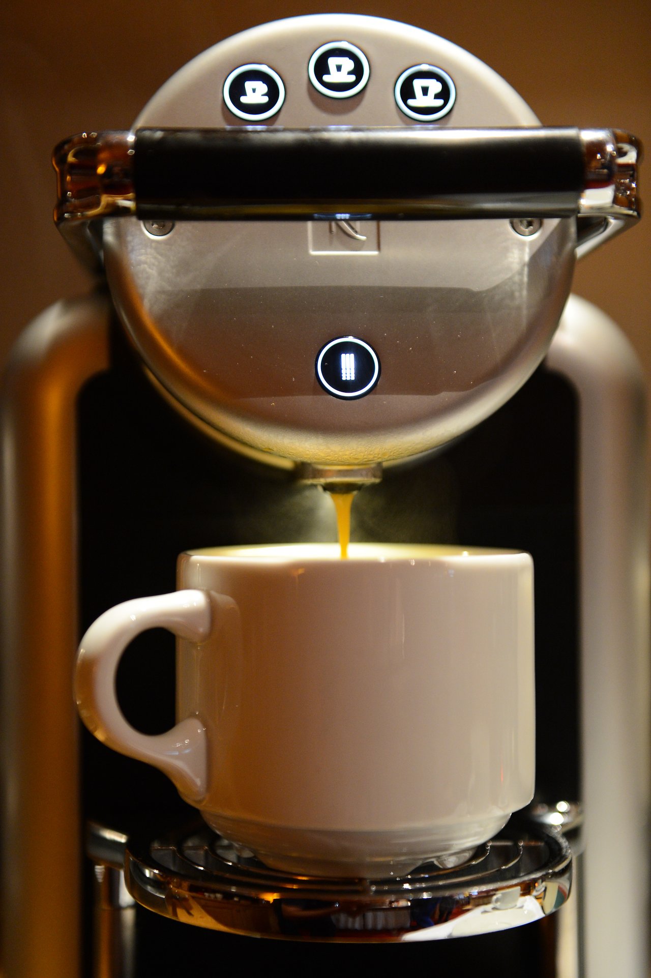 A coffee machine pours hot coffee into a white mug placed on its drip tray.