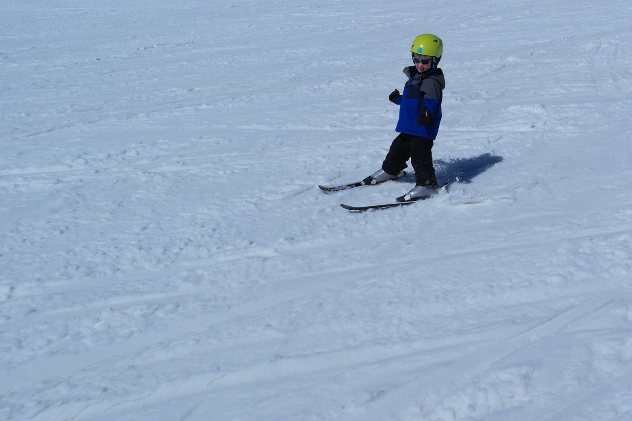A child wearing a helmet and ski gear is skiing on a snowy slope.