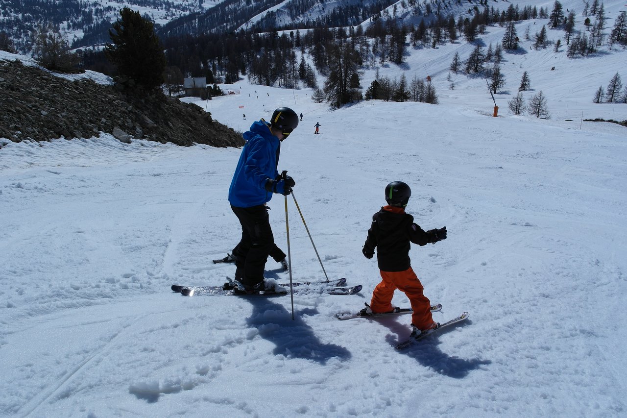 An adult and a child wearing helmets ski together on a snowy slope.