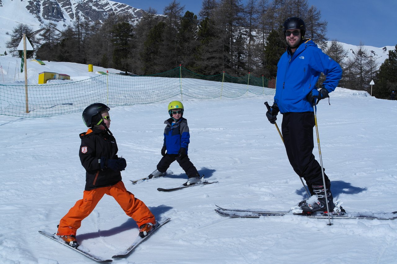An adult and two children wearing helmets and ski gear practice skiing on a snowy slope.