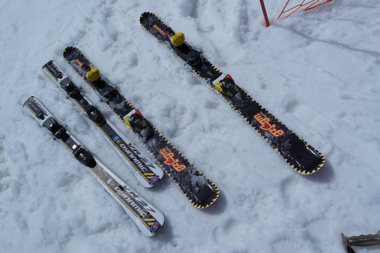 Four skis with bindings are lying on the snow, two with a black and yellow design and two white.