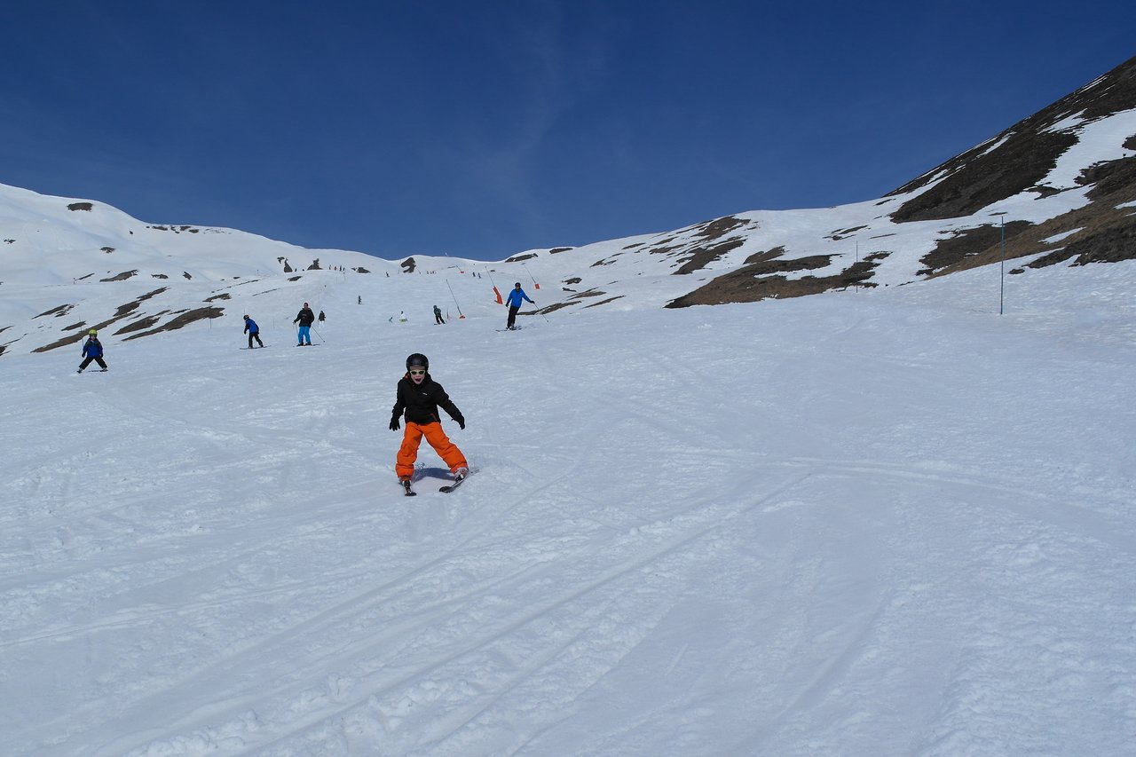 A person in orange pants skis down a snowy slope, with several other skiers in the background.