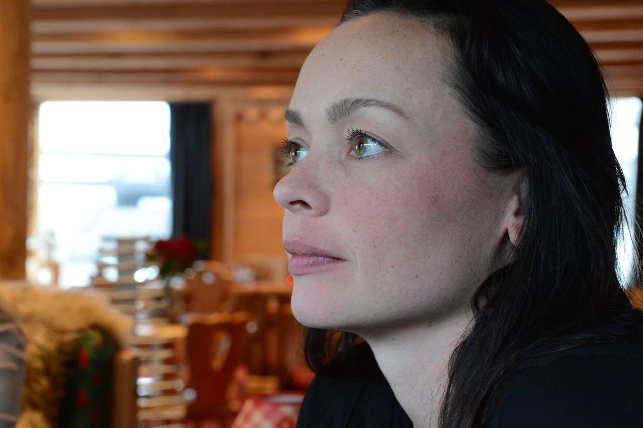 A woman with dark hair looks to the side in a warmly lit indoor setting.