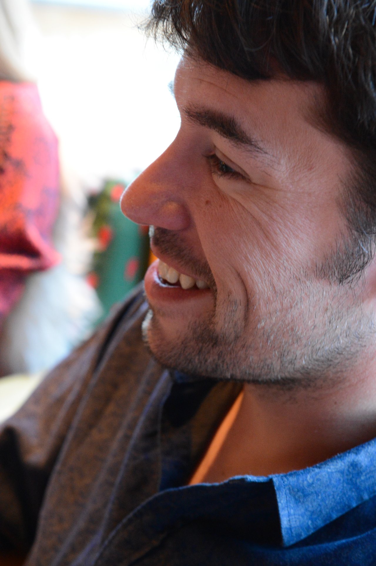 A man with short dark hair and a beard smiles while looking to the side.