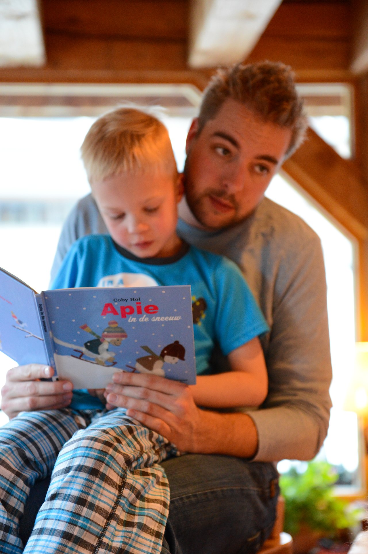 A man and a young child sit together, reading a children's book about winter.