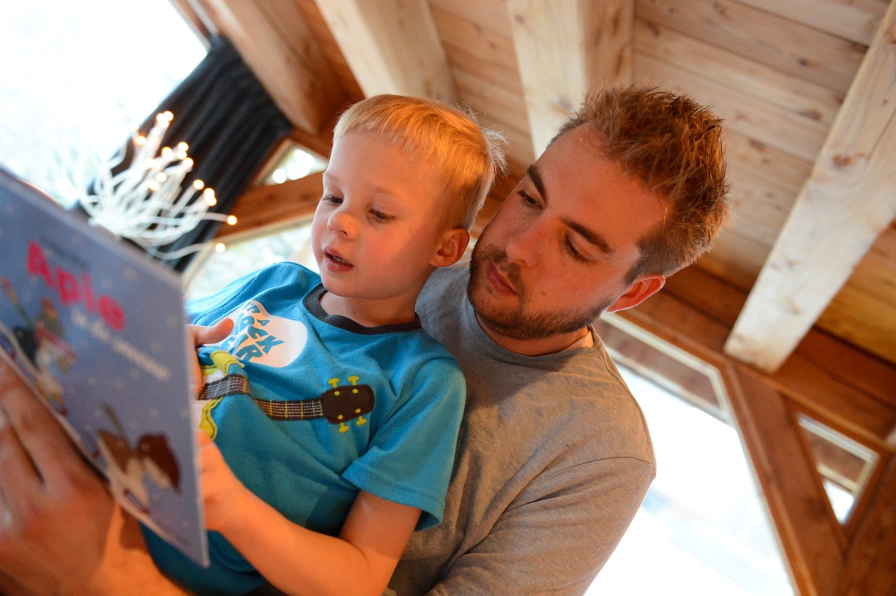 A man and a young child sit together, reading a colorful children's book.