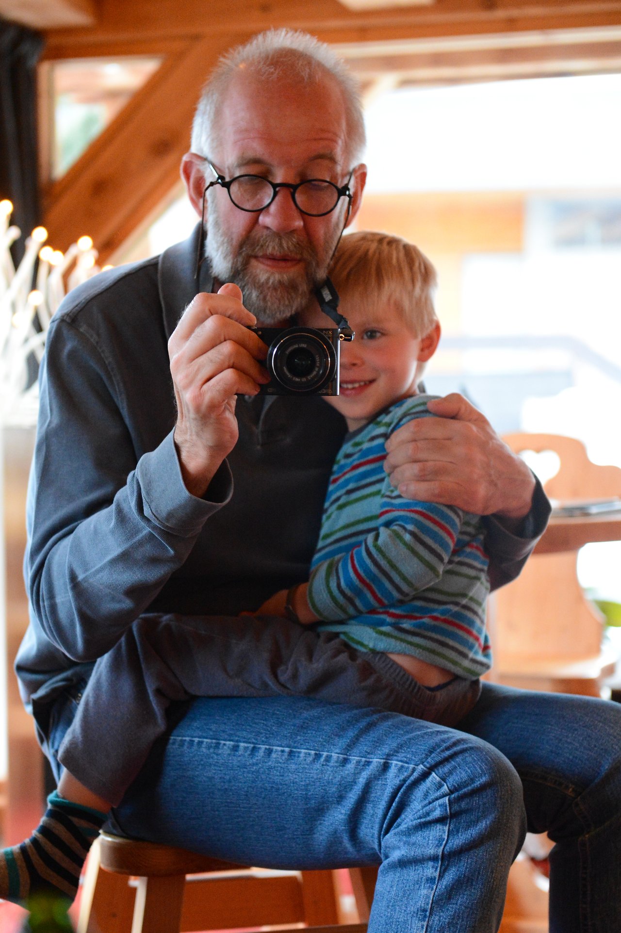 An older man with glasses holds a camera while a young child sits on his lap, smiling.
