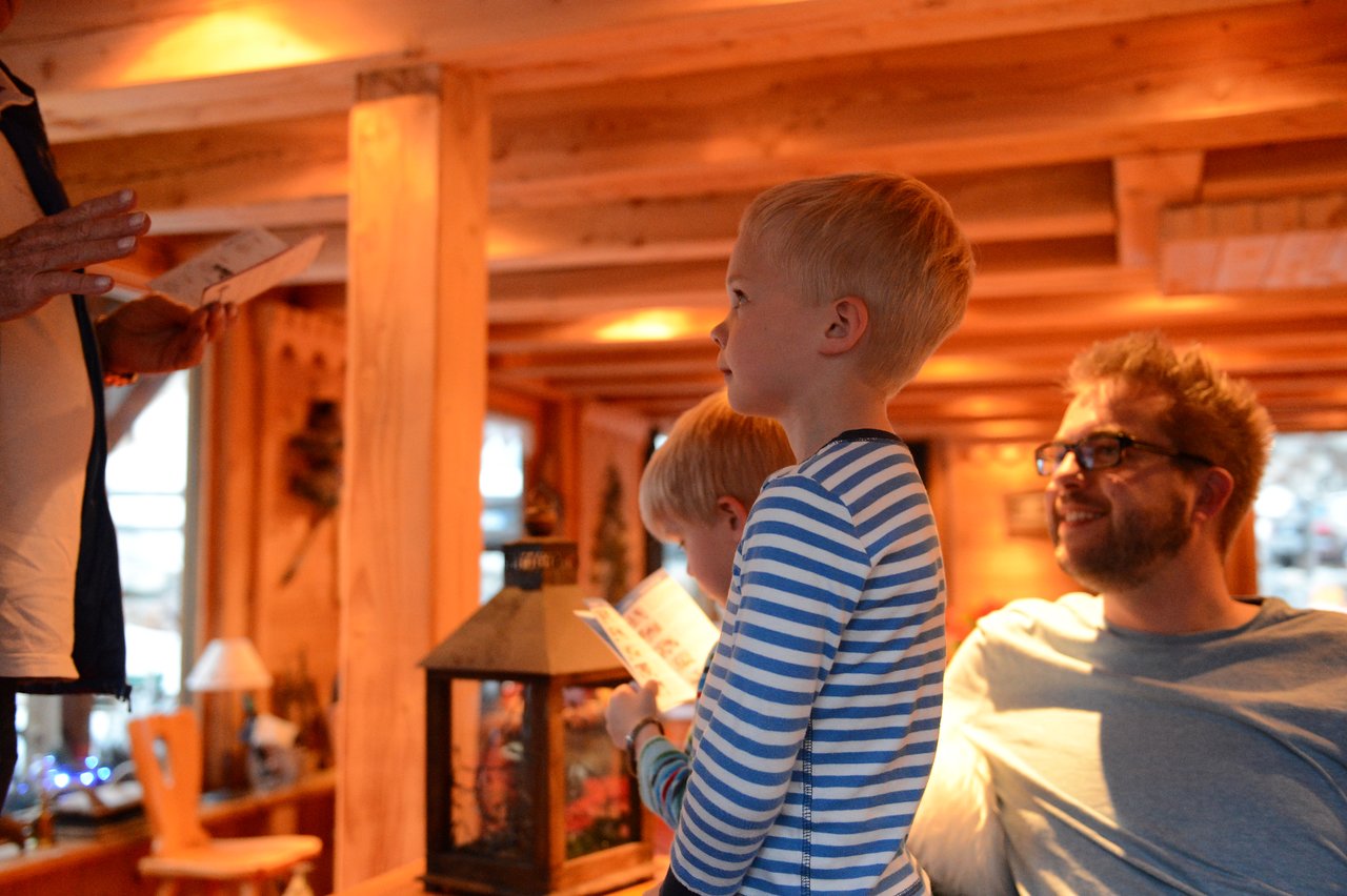 A child in a striped shirt stands holding a paper, while an adult nearby smiles and watches.