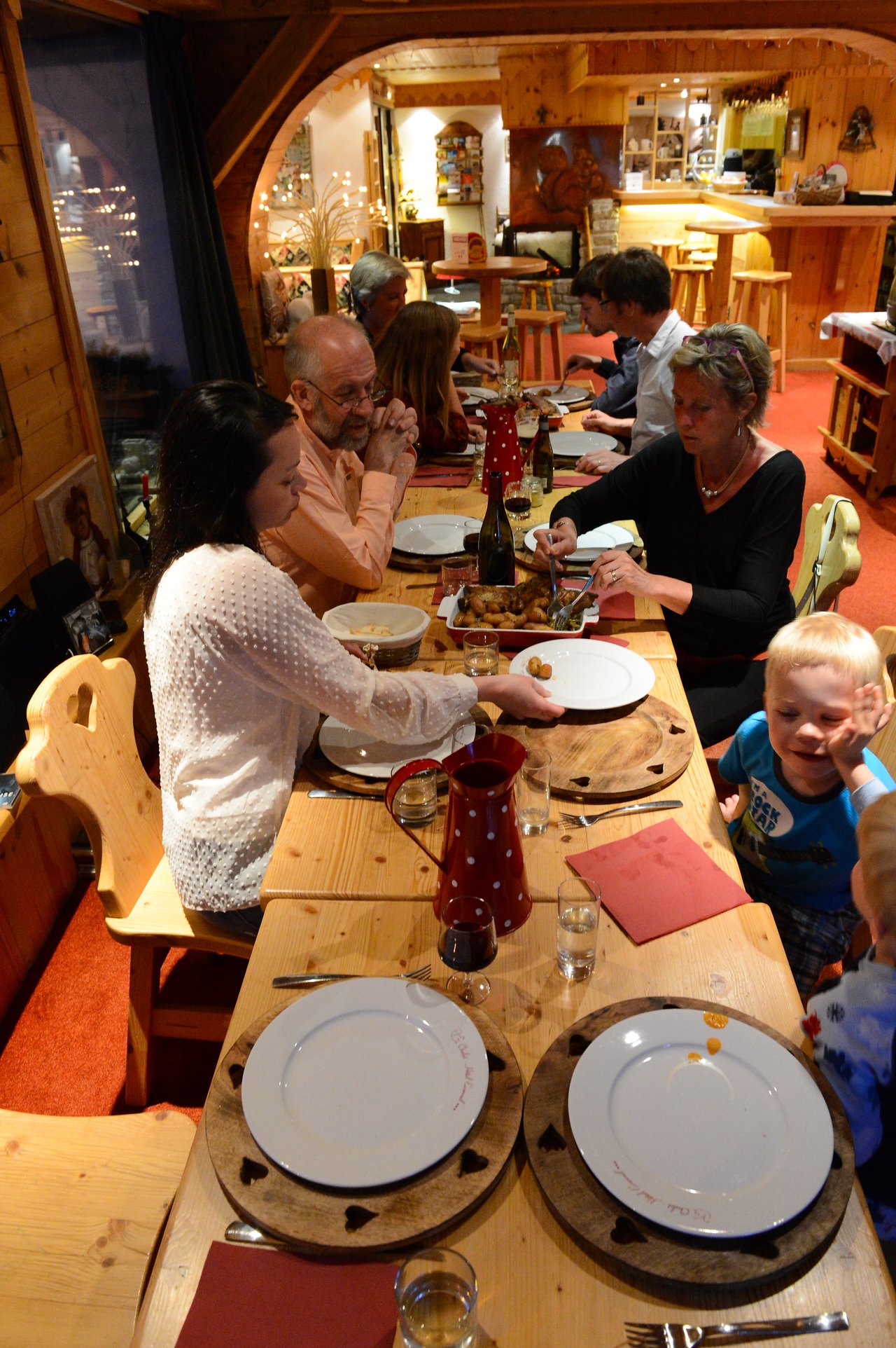 A group of people sits around a wooden table, sharing a meal in a cozy restaurant setting.