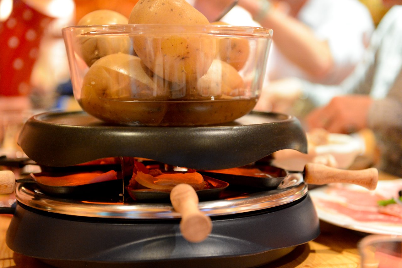 A raclette grill with cheese melting in small pans and a bowl of potatoes on top.