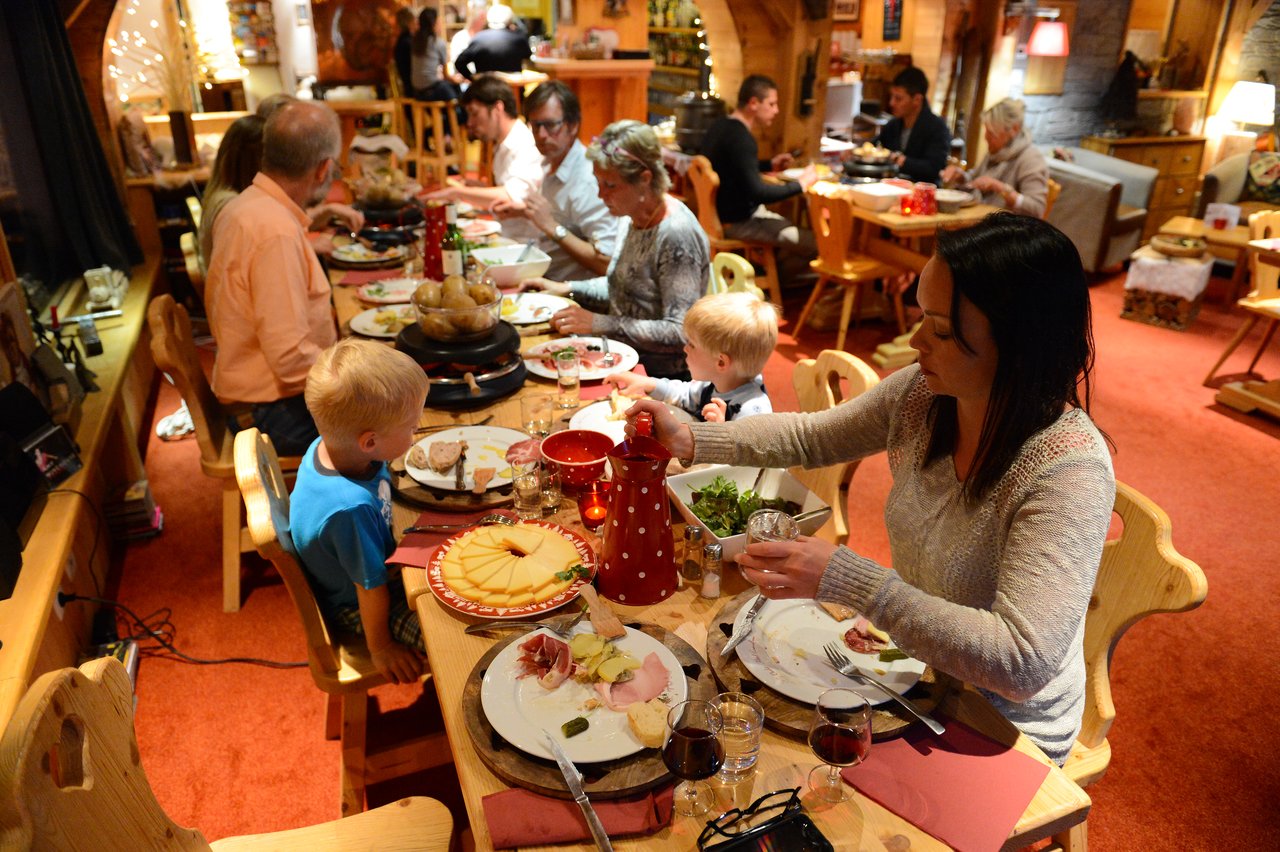 People gathered around a wooden table in a cozy restaurant, sharing a meal with cheese, meat, and wine.