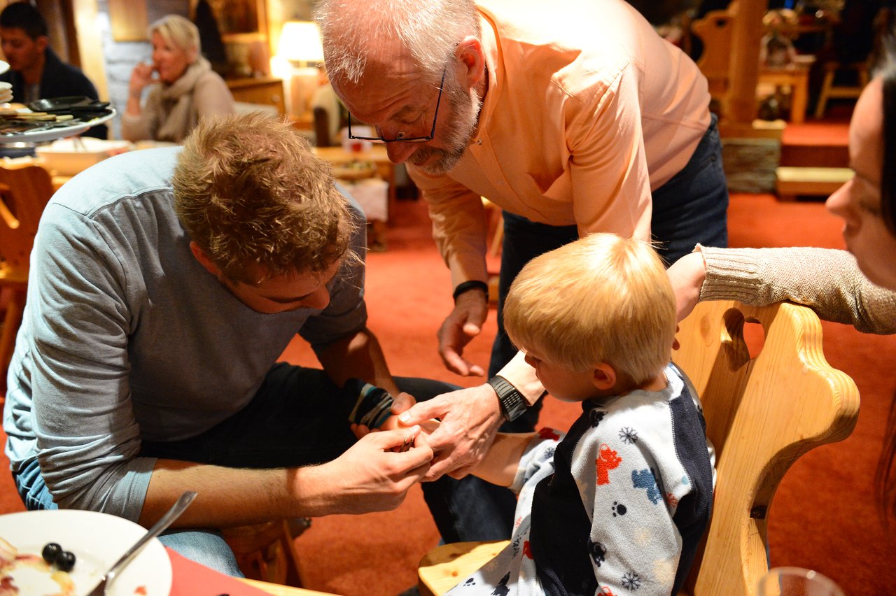 A man examines a young child's hand while an older man and a woman assist in a warmly lit setting.