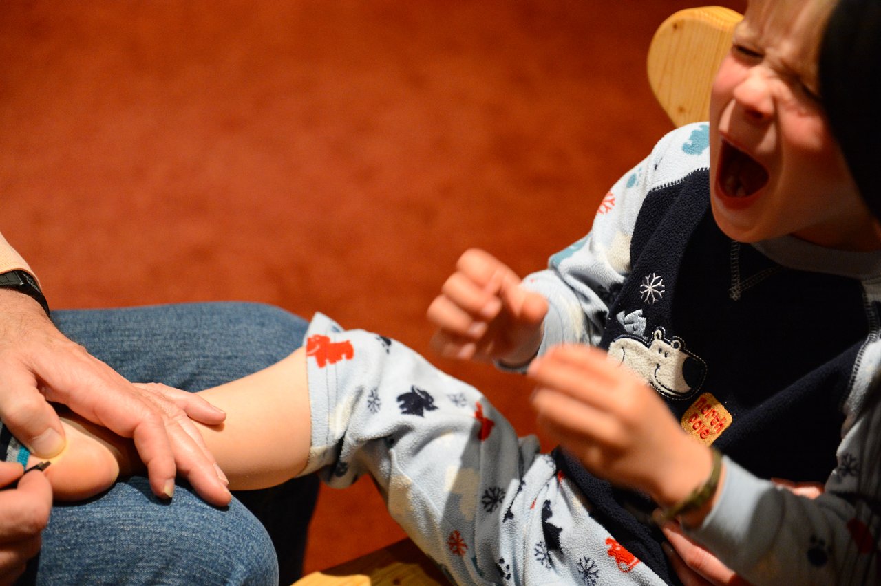 A child in pajamas cries while an adult tends to their injured foot with a bandage.