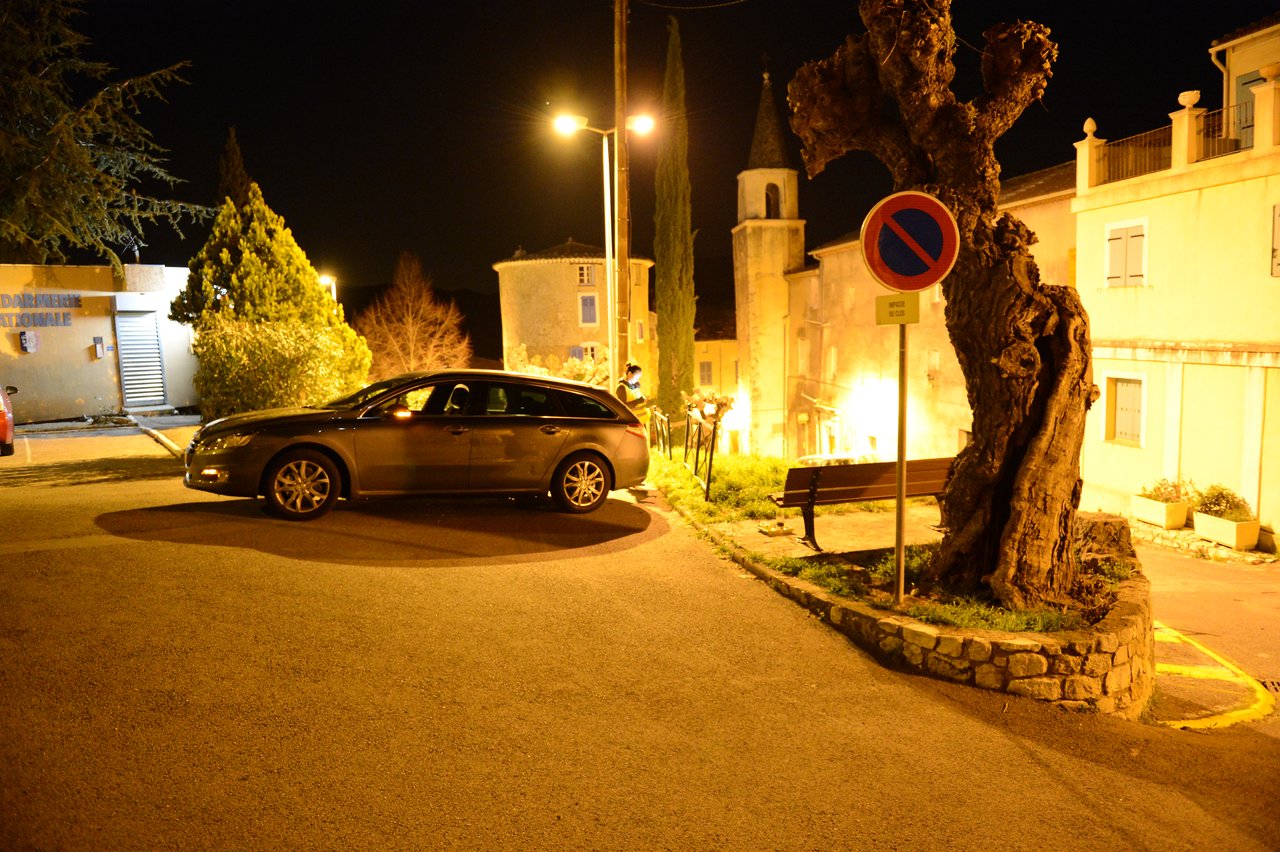 A parked car on a street at night, with a no-parking sign and illuminated buildings in the background.