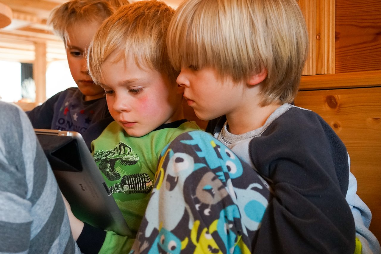 Three children sit closely together, focused on a tablet screen.