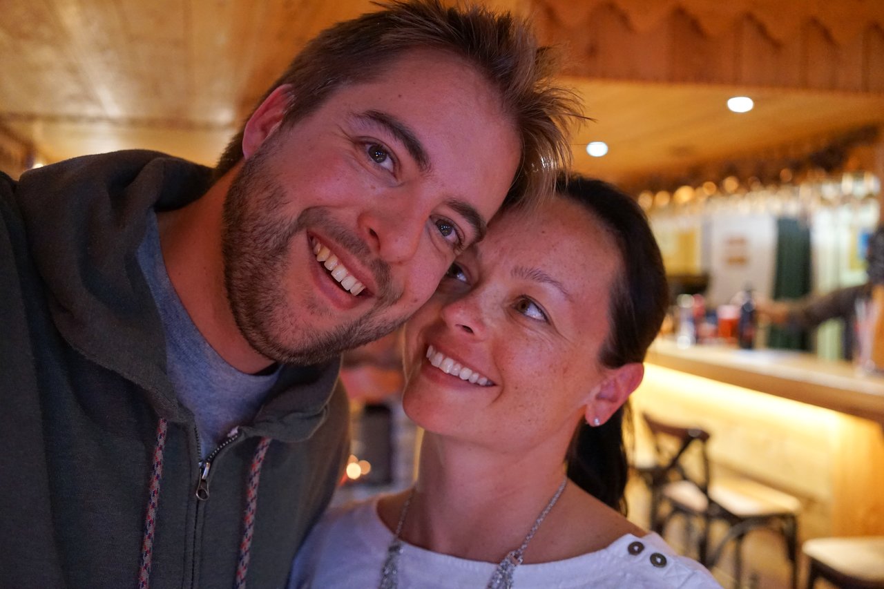 A smiling man and woman pose closely together in a warmly lit bar or restaurant.