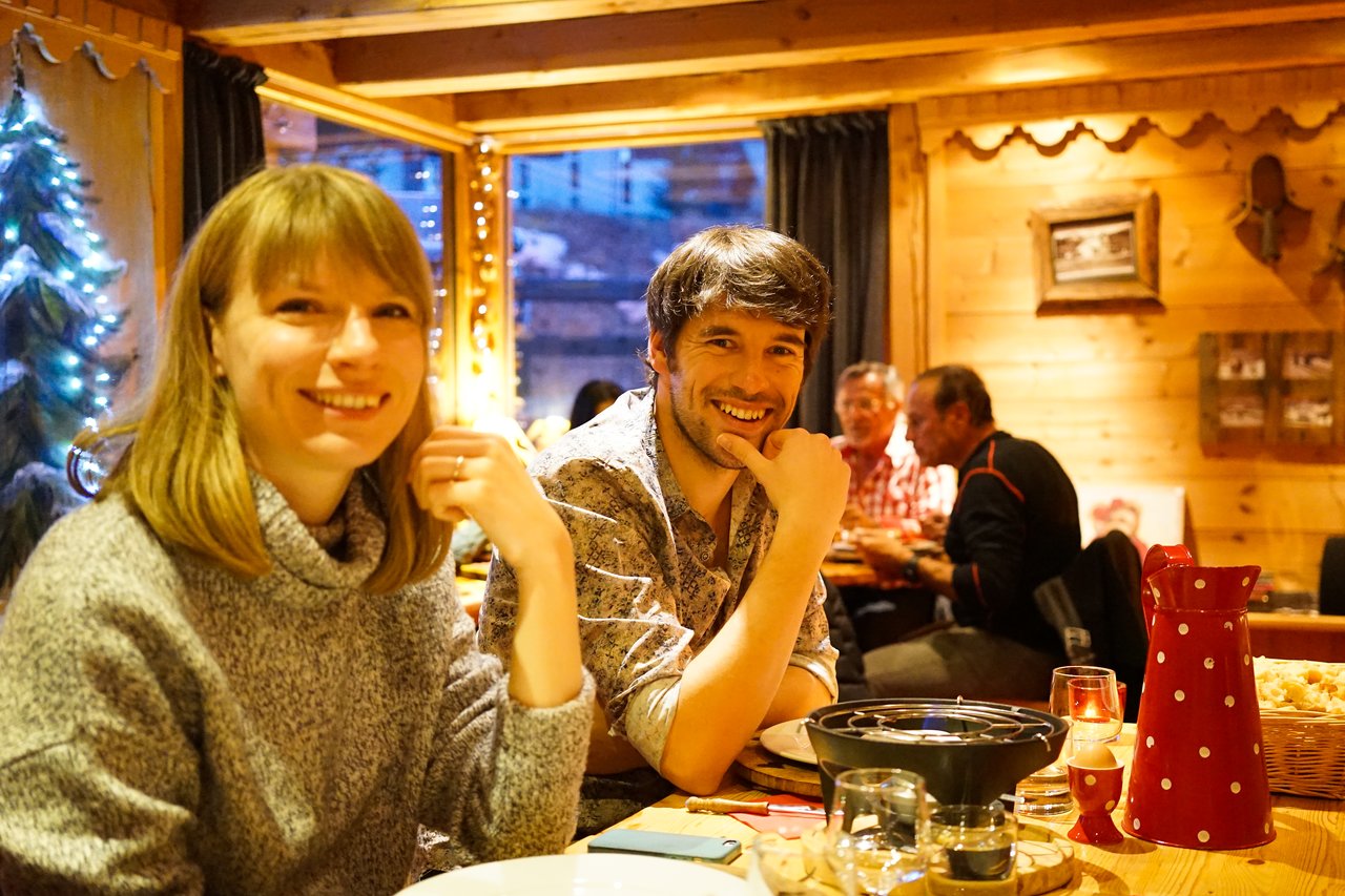 A smiling man and woman sit at a wooden table in a cozy restaurant, enjoying a meal together.