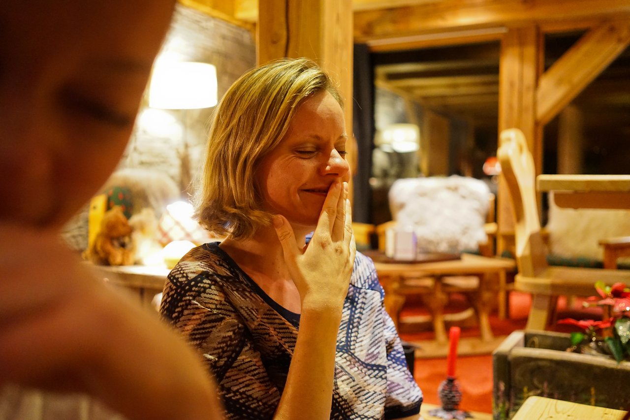 A woman with short blonde hair smiles with her eyes closed, touching her face with her fingers.