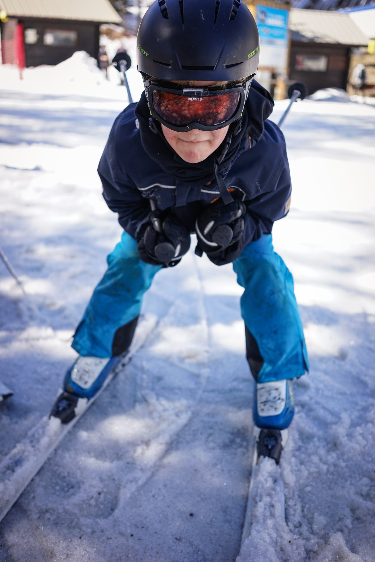 A skier in a helmet and goggles leans forward on skis, gripping poles, preparing to move on snowy ground.