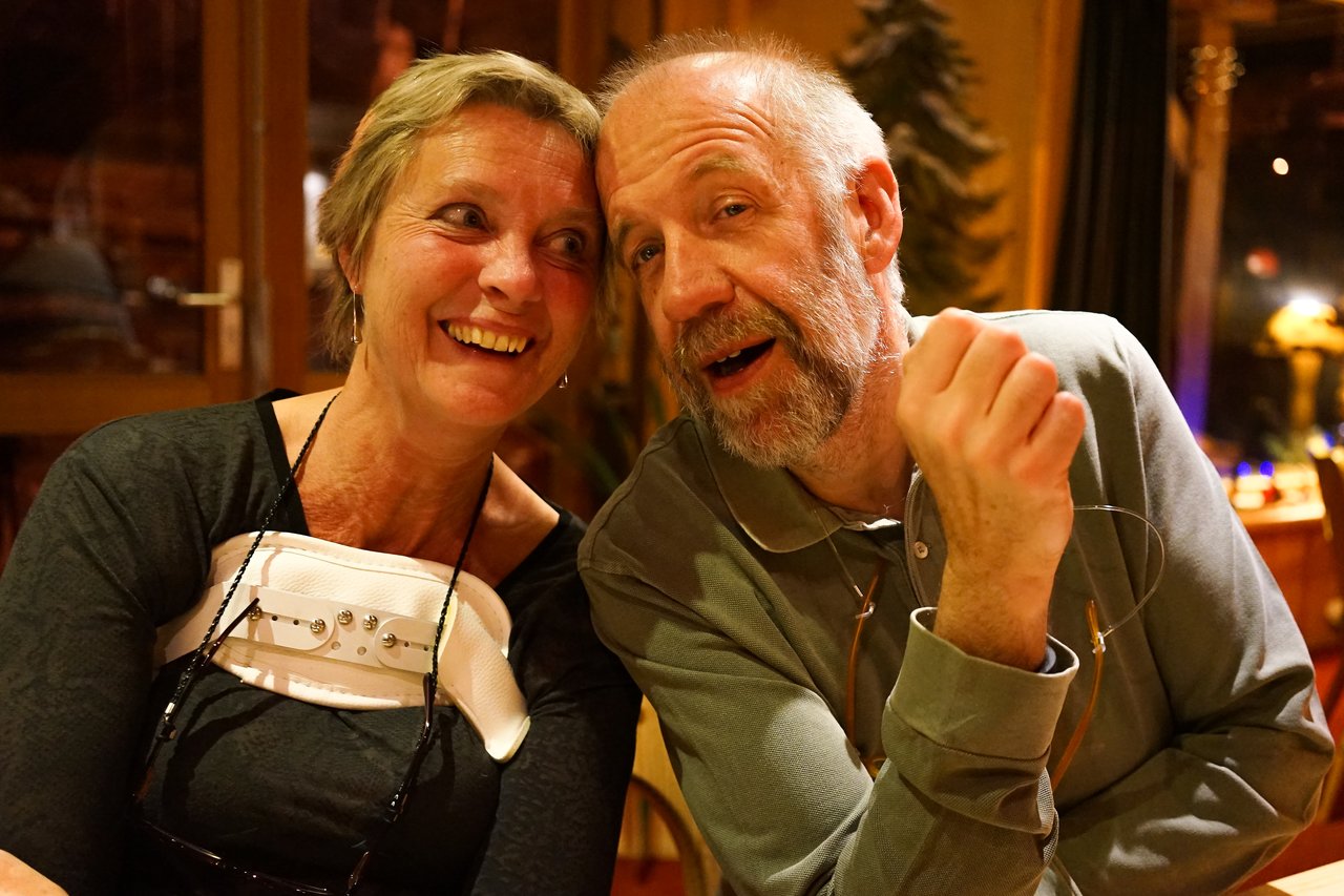 A smiling woman leans toward a bearded man who is speaking and gesturing with his hand in a warm setting.