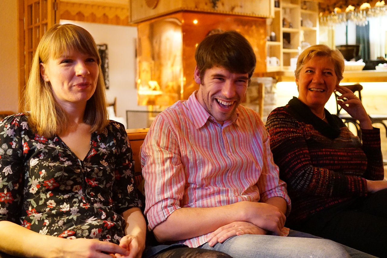 Three people sitting together indoors, smiling and laughing.