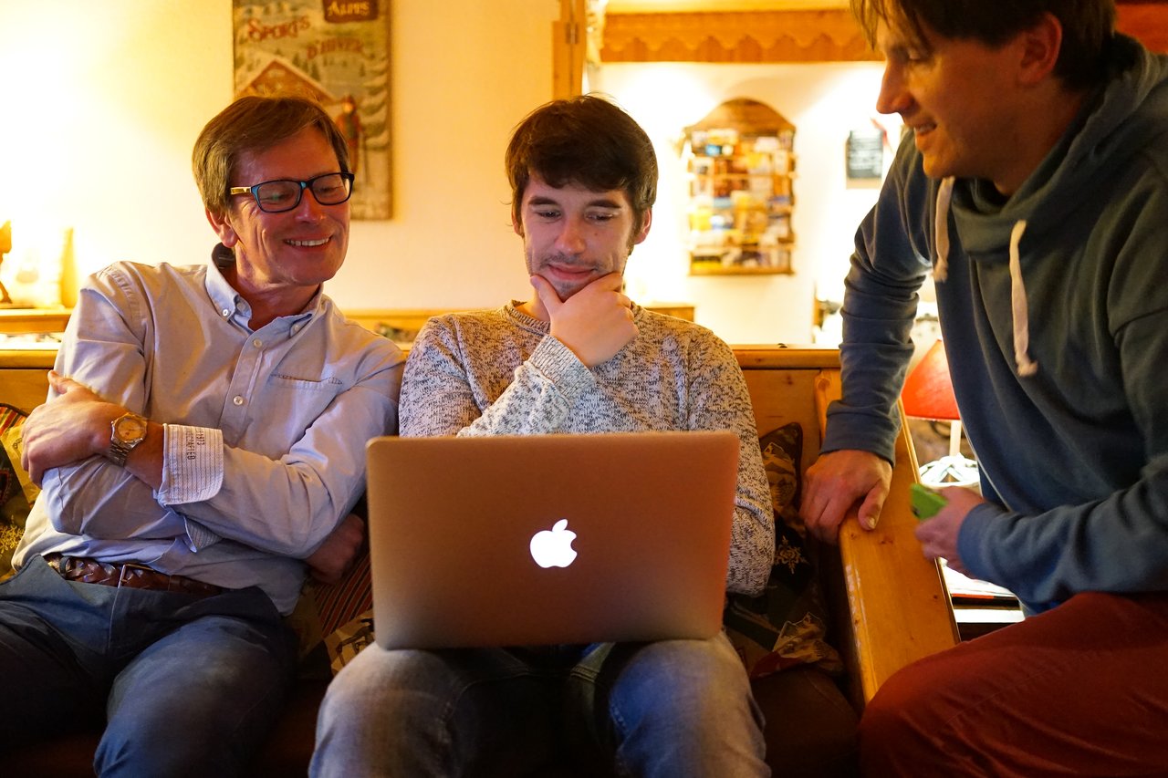 Three people sit on a couch, looking at a laptop screen.
