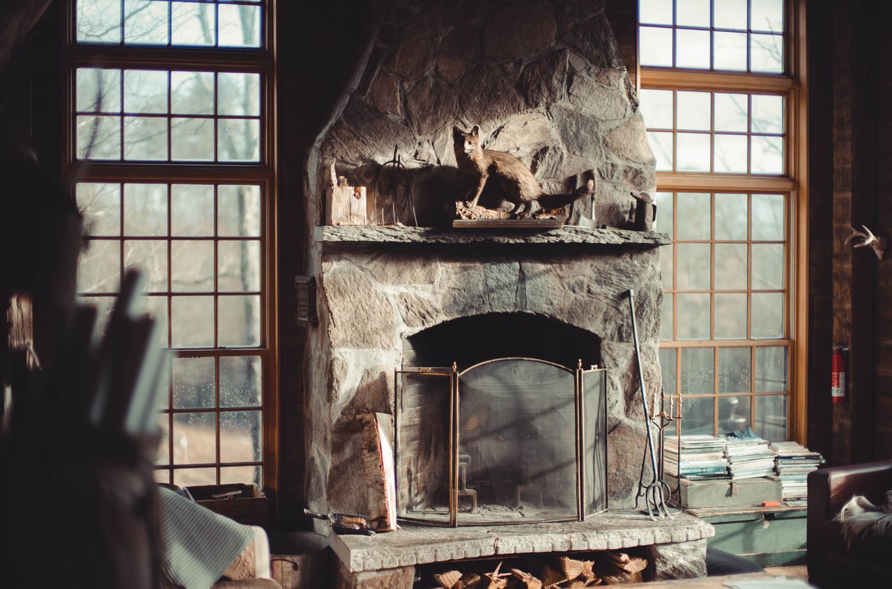 A stone fireplace with a taxidermy fox on the mantel, surrounded by large windows and rustic decor.