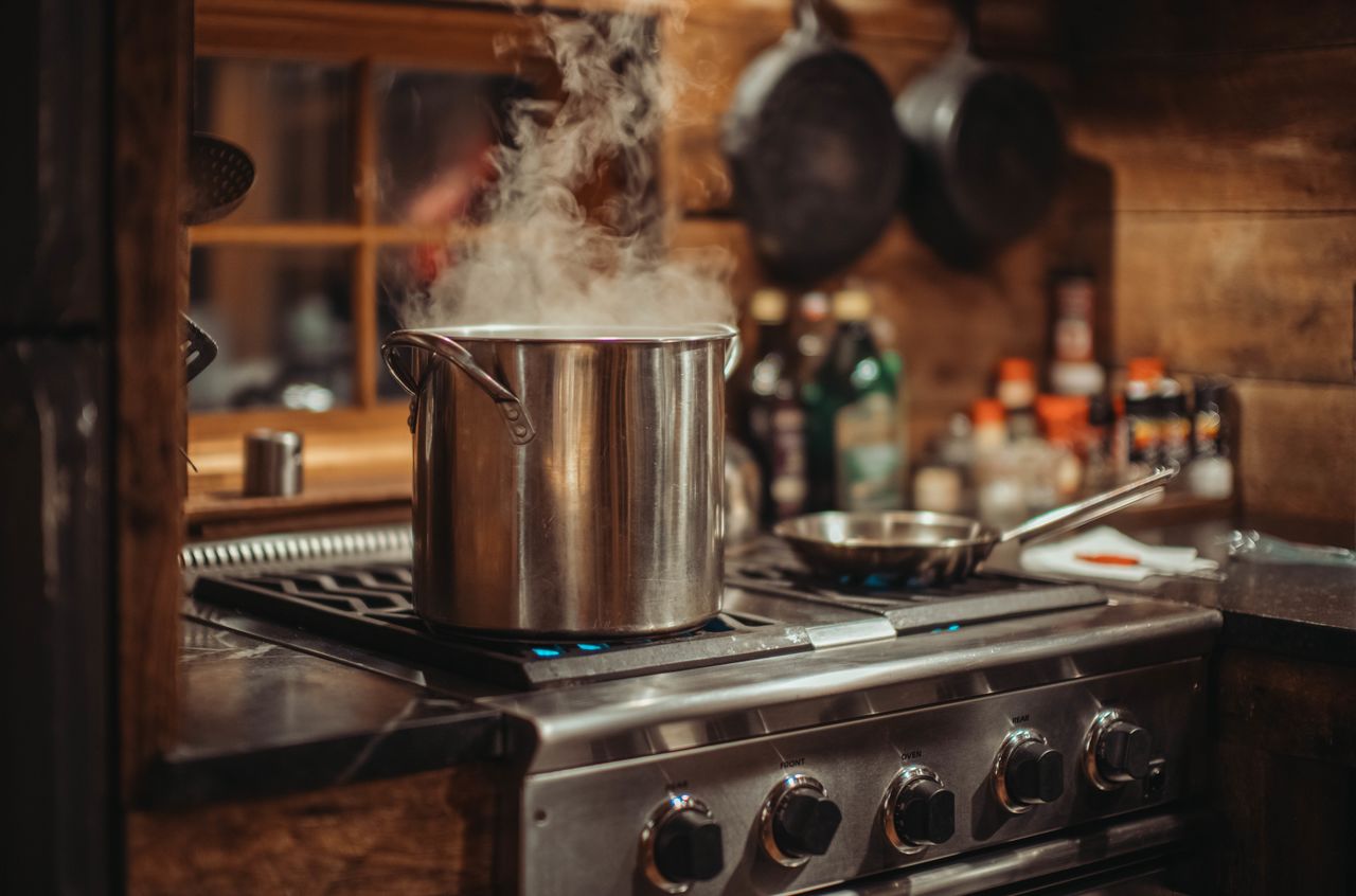 A steaming pot sits on a stove in a cozy kitchen, with spices and cookware in the background.
